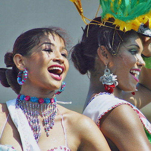 Two joyful Colombian women in white dresses and colorful accessories smiling and performing during the Barranquilla Carnival