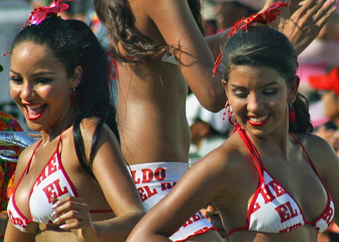 Dancing Women in Barranquilla Carnival Parade Two smiling Colombian women in red and white carnival outfits dancing joyfully during the Barranquilla Carnival parade