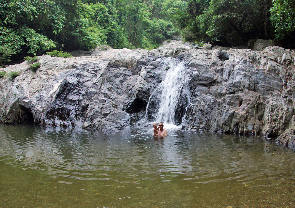 Father and two year old daughter alone in a swimming hole with a small waterfall