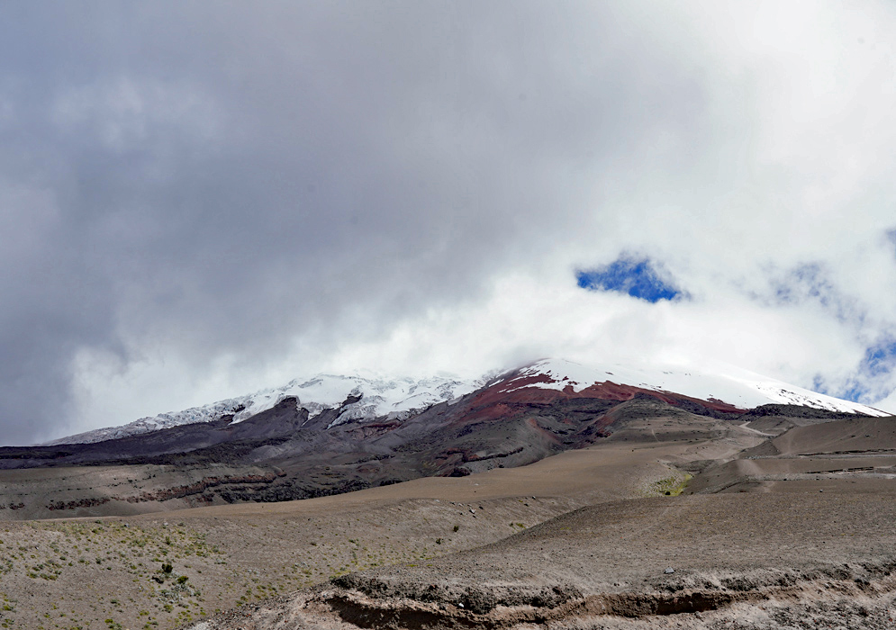 Volcanic Majesty of Cotopaxi Cotopaxi volcano capped with snow and red volcanic rock looms over a vast, open grassland