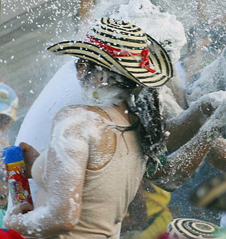 Carnival participants playfully spraying foam on each other, with a woman in a traditional hat covered in white foam during Barranquilla Carnival